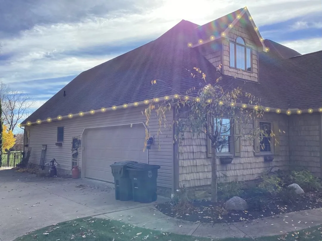 Warm-white lights traced neatly along a home's roofline on a sunny day