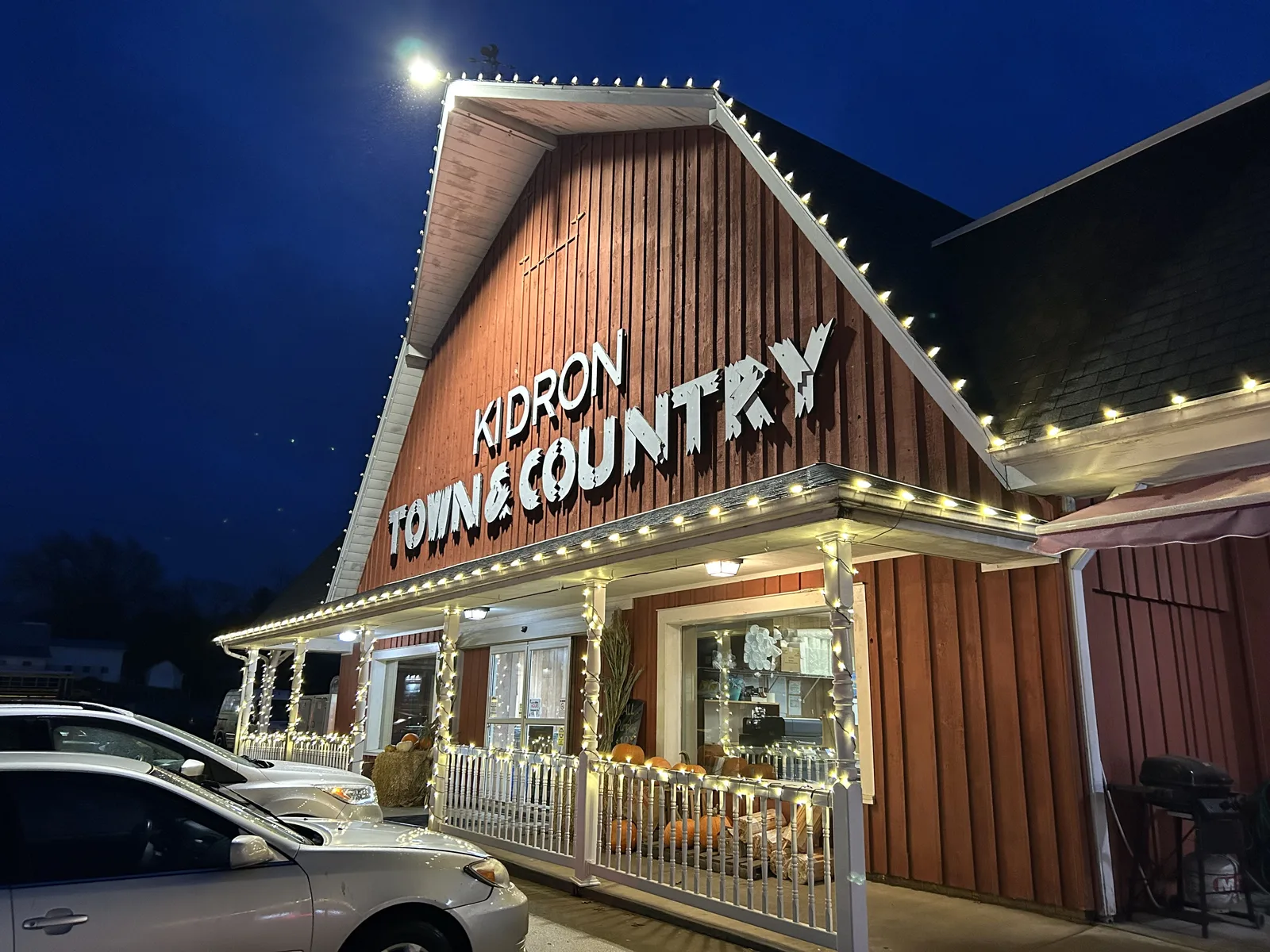 Kidron Town & Country barn outlined in warm-white Christmas lights at dusk