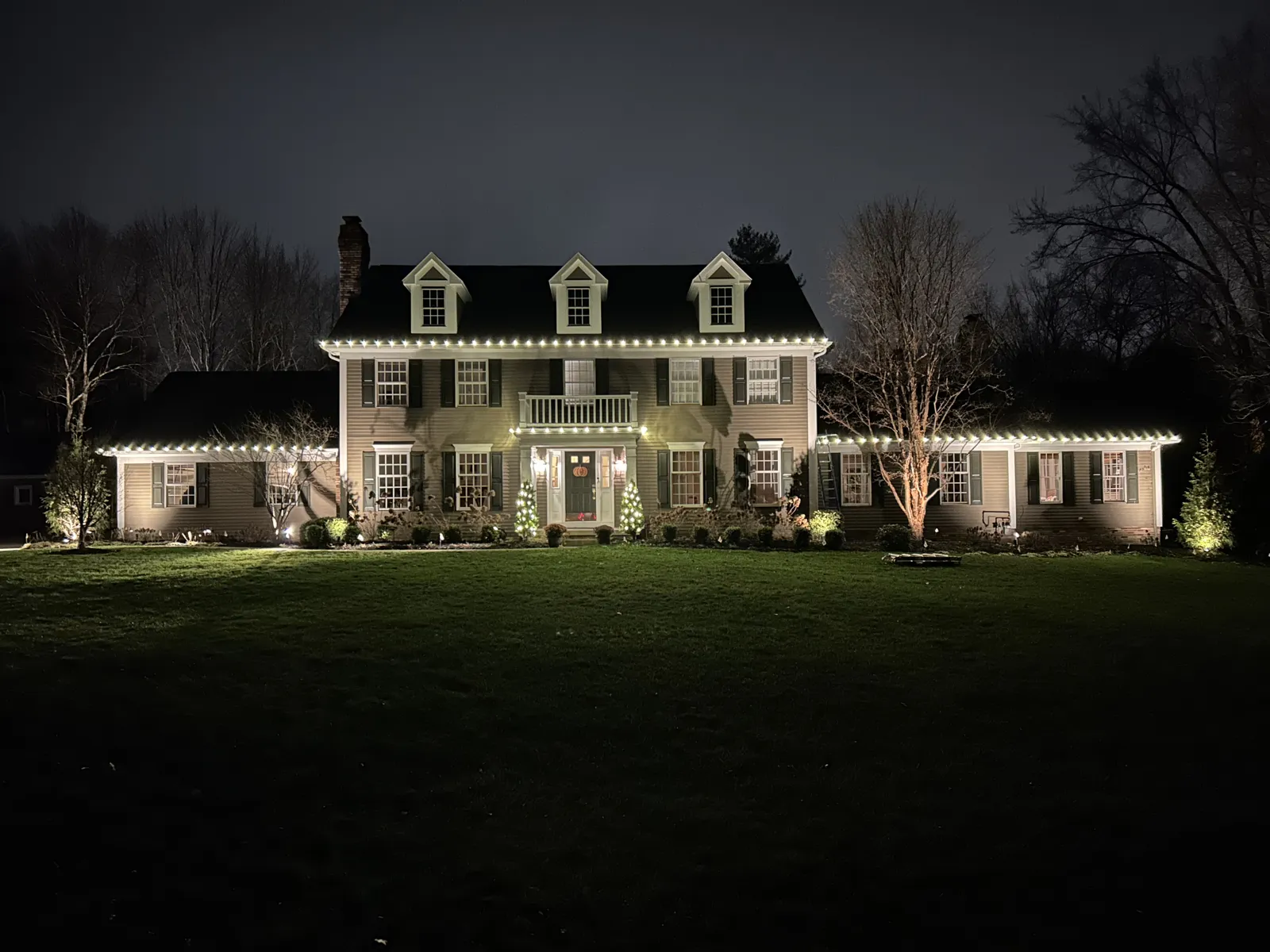 Large colonial home fully outlined in warm-white Christmas lights at night