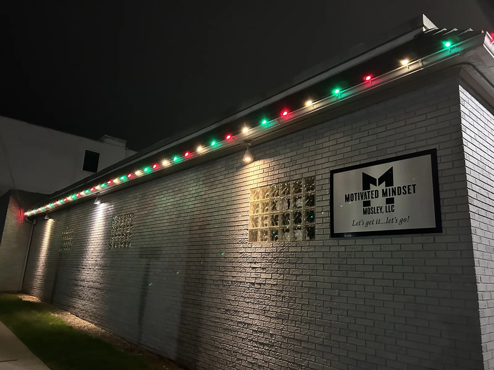 Red and green Christmas lights mounted along a brick wall at night
