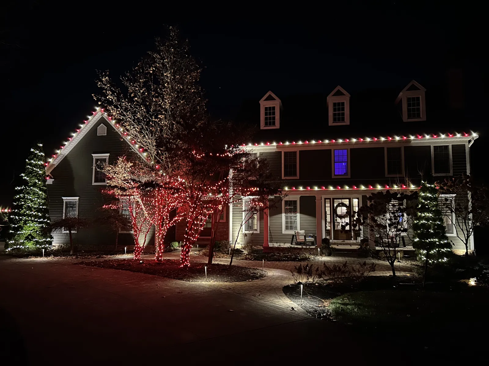 Red-wrapped tree beside a colonial home with red and white roofline lights
