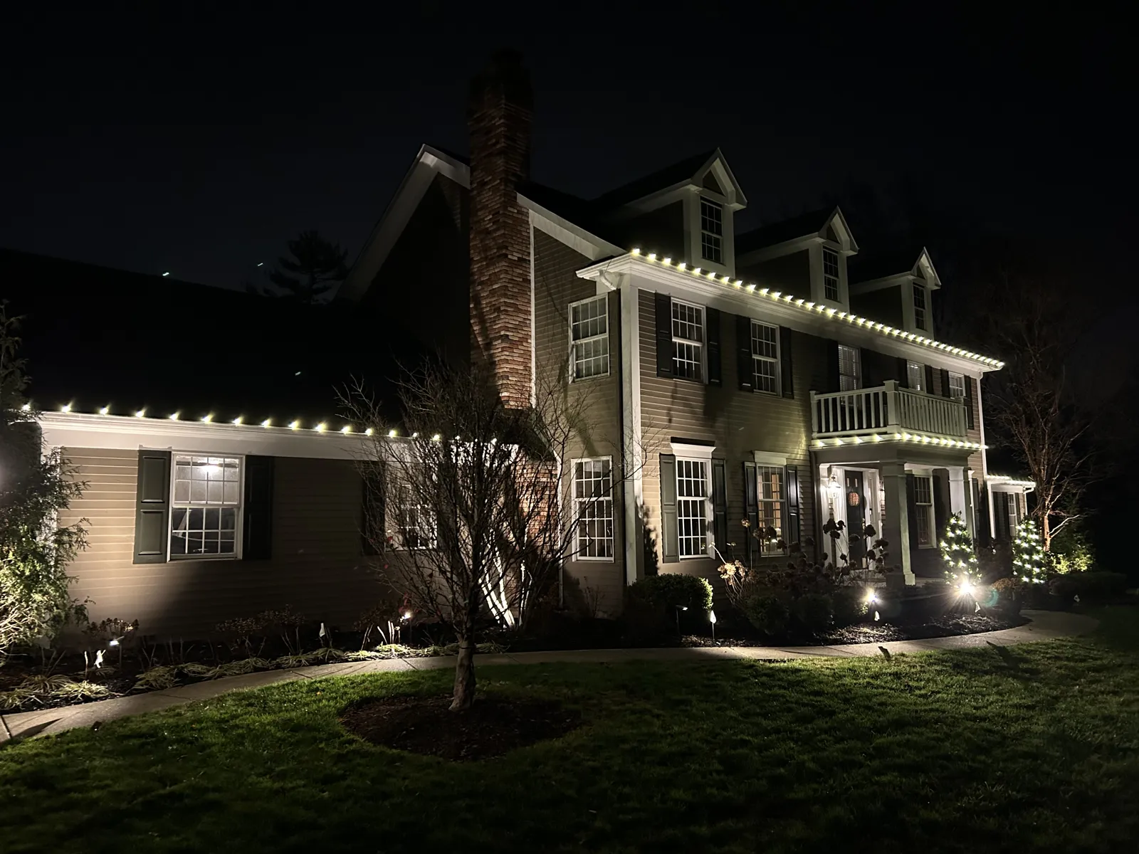 Colonial home with warm-white lights tracing every roofline and dormer