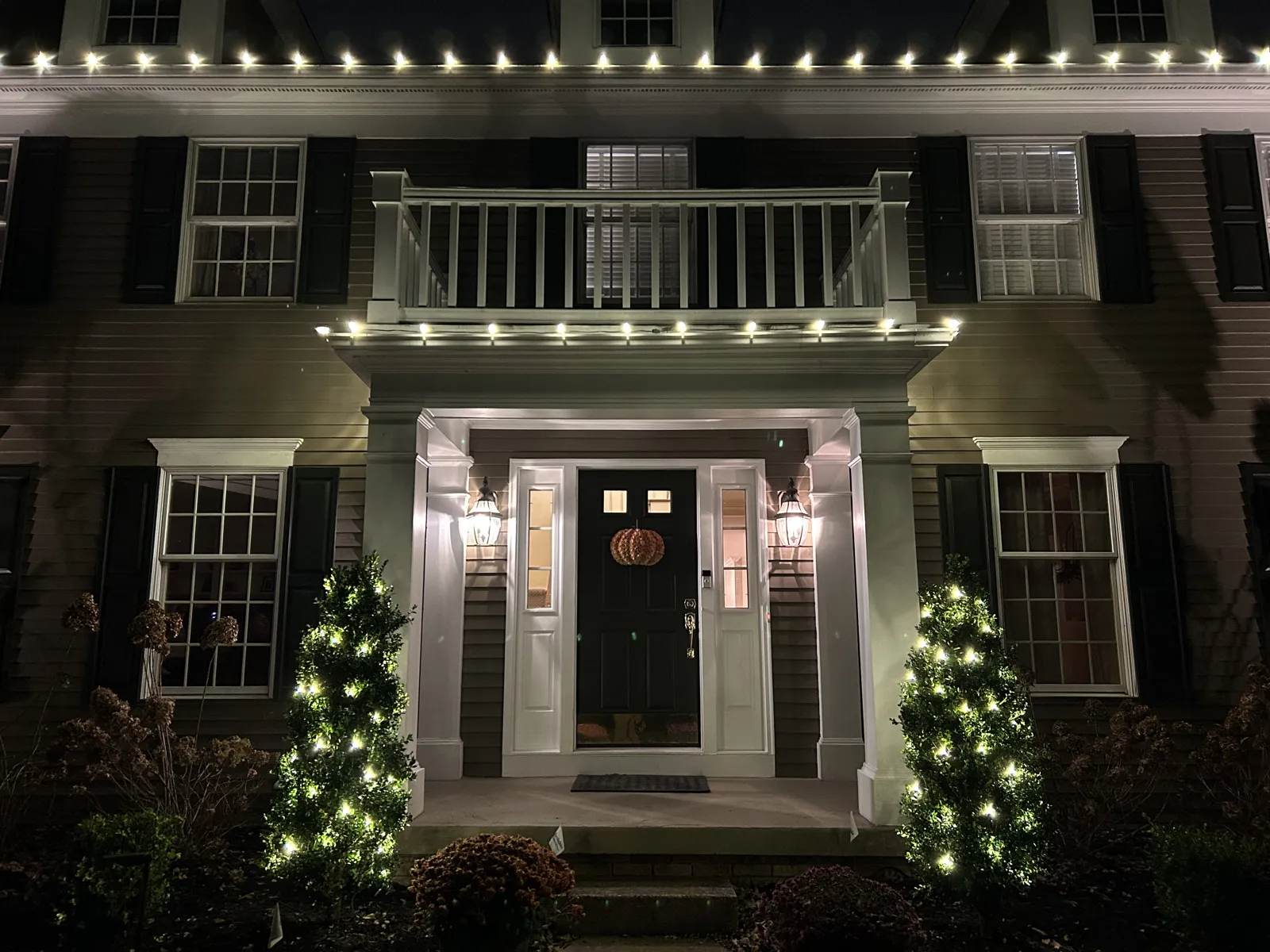 Colonial entry with warm-white roofline lights and two lit evergreens
