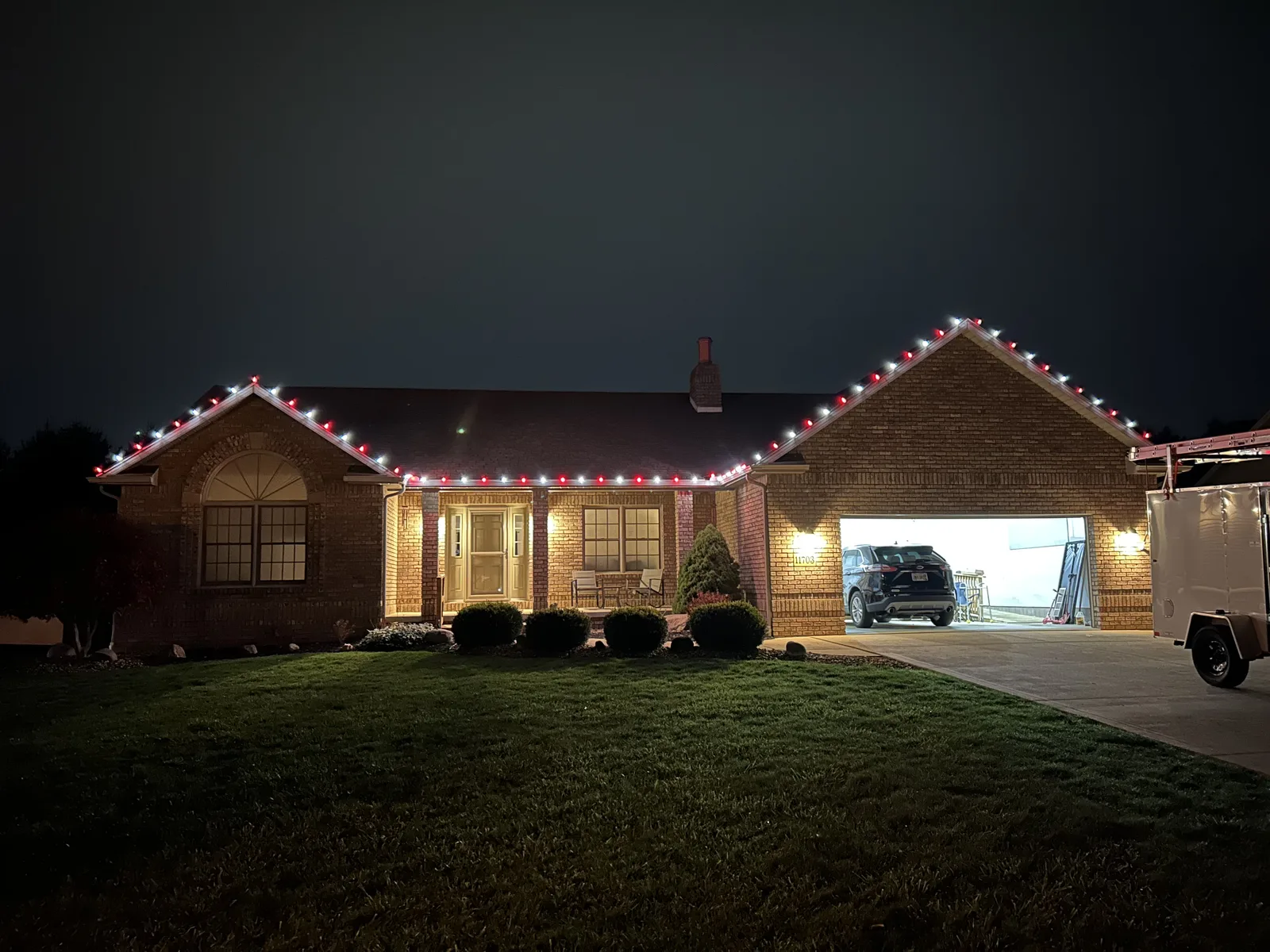 Brick home with warm-white roofline Christmas lights and lit garage at night