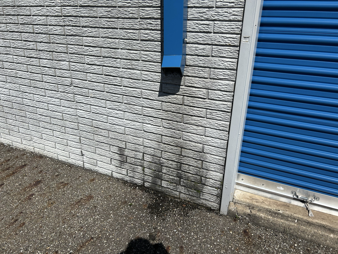 Storage facility exterior below a gutter outlet showing drainage staining
