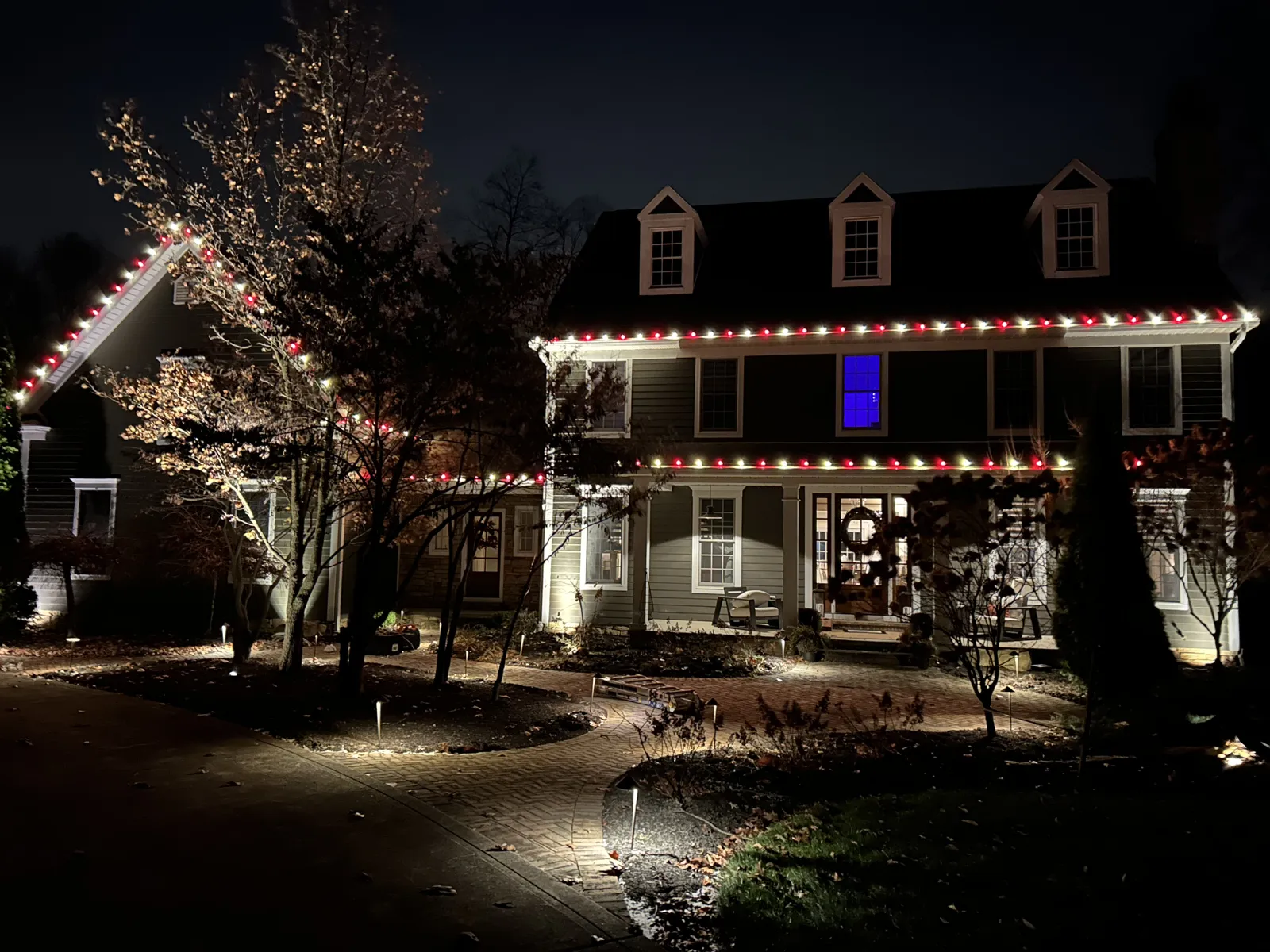 Colonial home with red and white roofline lights and lit landscaping