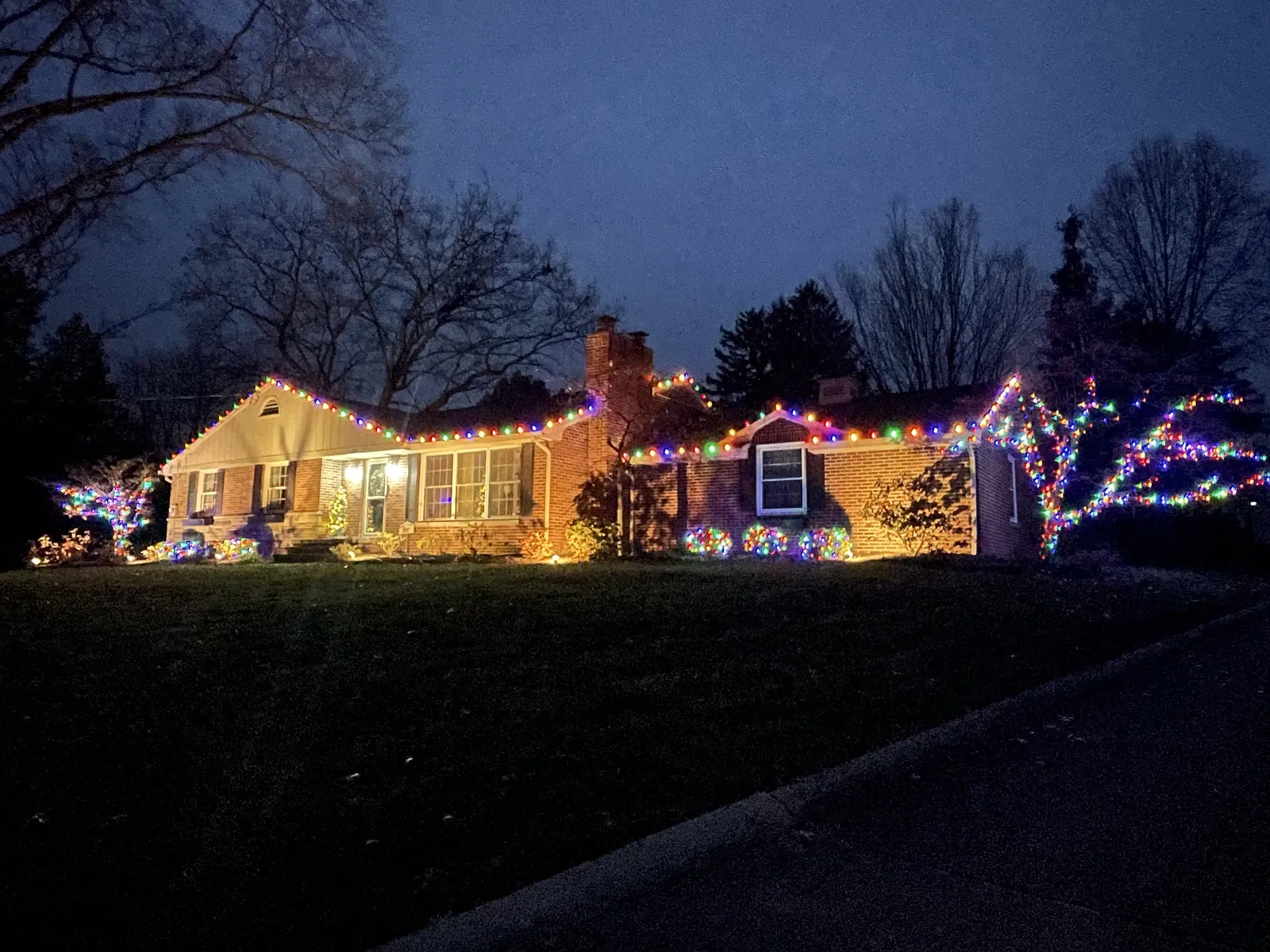Ranch home with multi-color roofline and bush lights at dusk