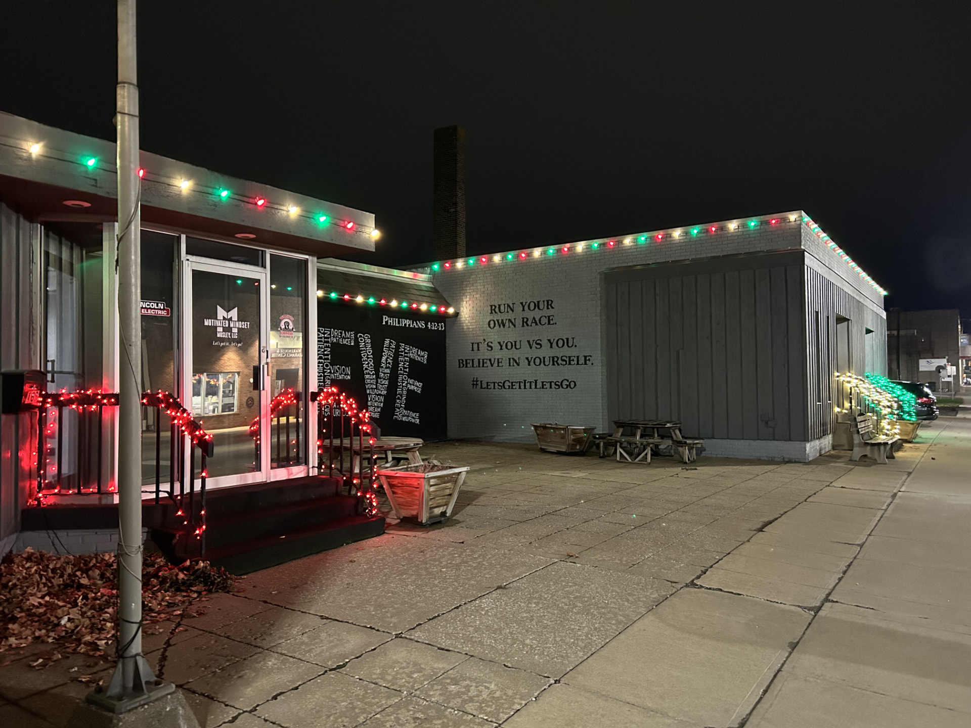 Storefront outlined in red, green, and warm-white Christmas lights with red-lit railings at night